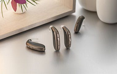 A display of Leox hearing aids on a light grey table with flowers in the background.